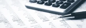 Close-up of a financial spreadsheet with numbers, calculator, and pen, representing county Medicaid work-verification and payment processing