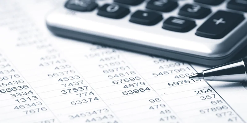 Close-up of a financial spreadsheet with numbers, calculator, and pen, representing county Medicaid work-verification and payment processing