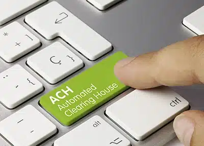 Close-up of a finger pressing an ACH button on a computer keyboard, symbolizing a merchant initiating a credit push payment under the 2026 Nacha Risk Management Framework