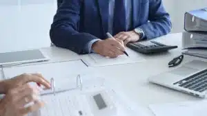 Utility finance professional in blue suit reviewing payment documents with calculator and laptop, analyzing credit card processing fees and cost recovery options