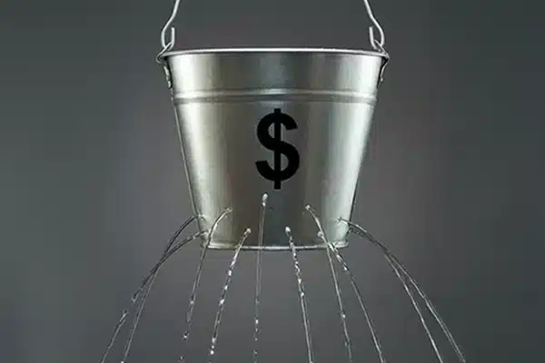 IP_utility-autopay-revenue-leak-mcc4900 A metal bucket with a dollar sign leaking water, representing unrecovered processing costs in utility AutoPay channels.