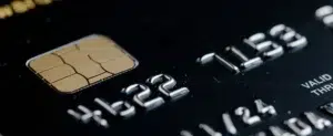 Close-up of a dark credit card showing the EMV chip and embossed numbers, representing secure digital payment processing
